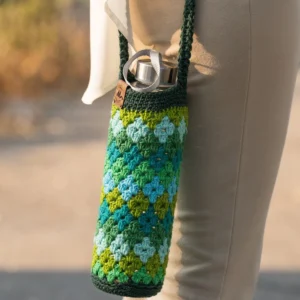Funda de crochet artesanal para botella de agua en tonos verdes y azules, con patrón de rombos, colgada en el hombro.