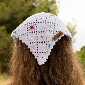 Pañuelo de crochet blanco hecho a mano con bordados de pequeñas flores de colores, visto desde atrás sobre cabello castaño, con etiqueta Marvicrochet.